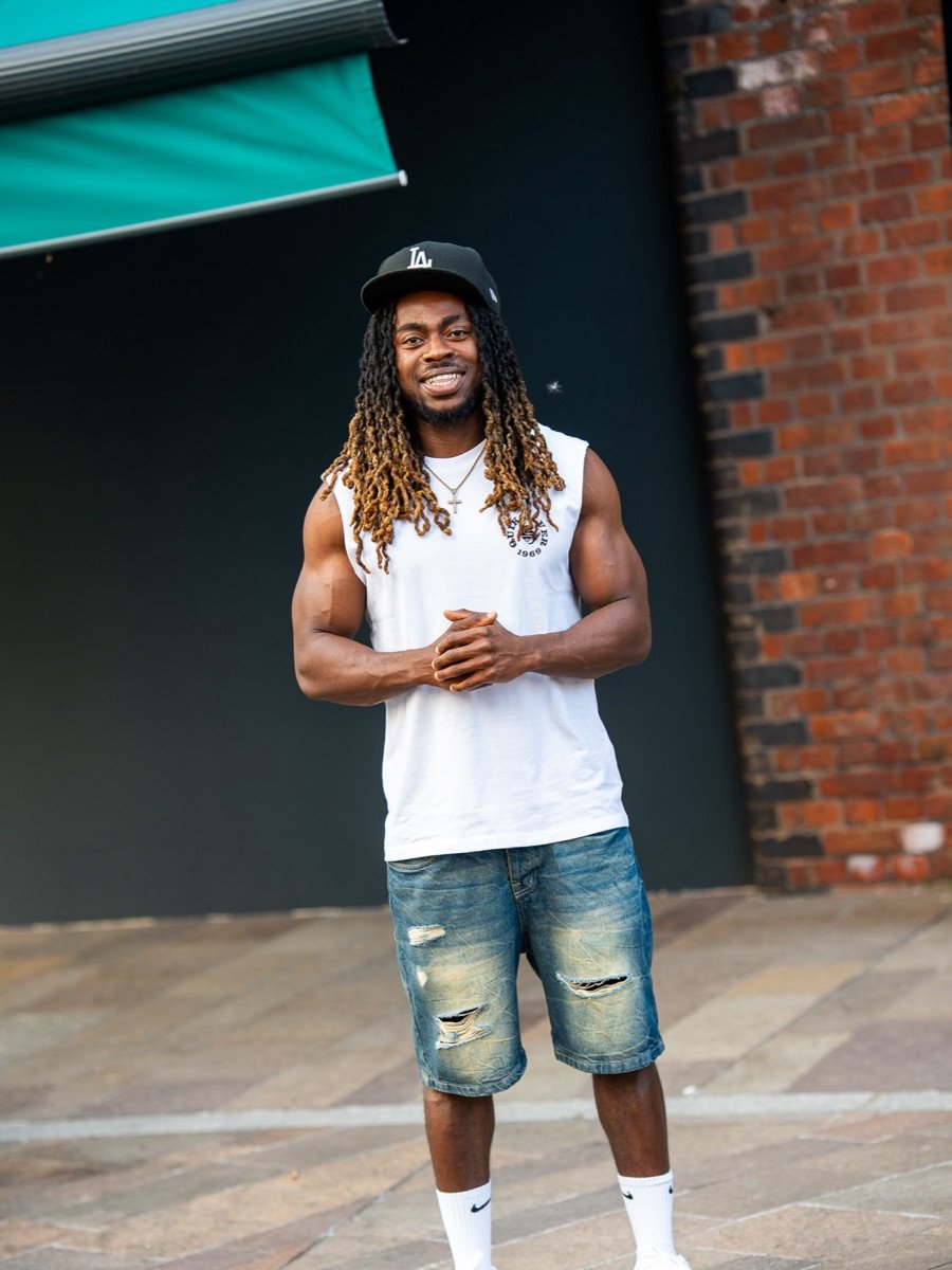Kunle Oduola standing outdoors in a white tank top and cap
