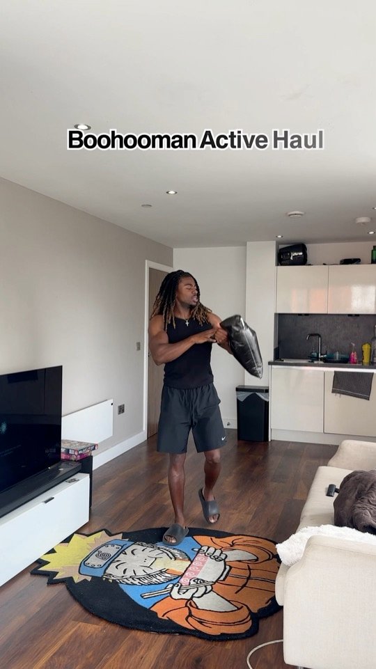 Still from a BoohooMAN reel: Kunle holding an activewear delivery package at home